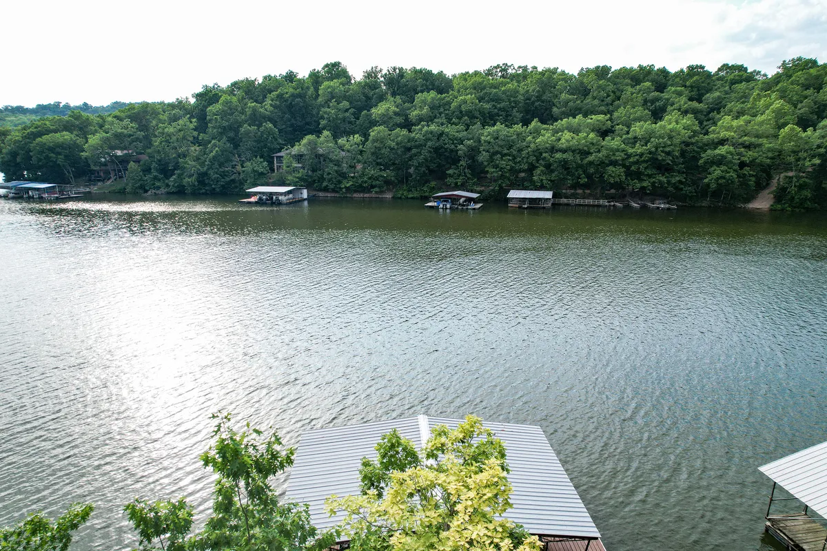A wide view of calm lake waters bordered by a green tree line, with several docks and boats visible in the distance. The serene atmosphere hints at peaceful water activities, sunset views, and wildlife sightings.