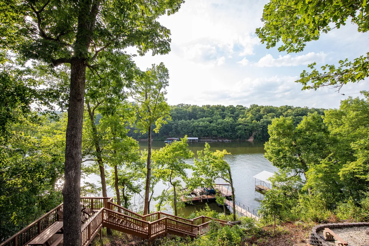 A scenic view featuring a sparkling lake, a wooden deck, lush green trees, and multiple docks. The landscape is open and inviting, perfect for walks, play, and wildlife watching with pets.