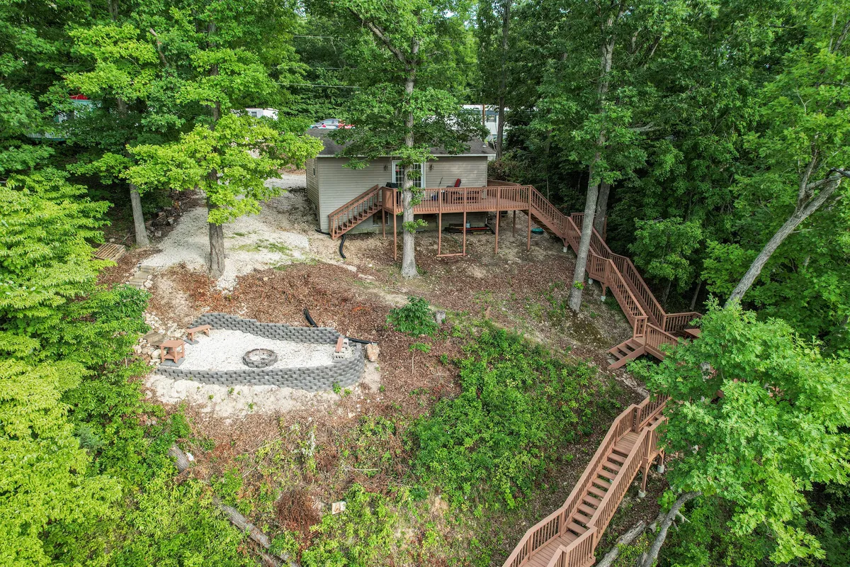 A view of the house nestled among trees, with a spacious deck and a fire pit in the foreground. The scene feels private and welcoming, emphasizing the retreat's location in the woods. The fire pit area suggests evenings spent storytelling or relaxing under the stars.