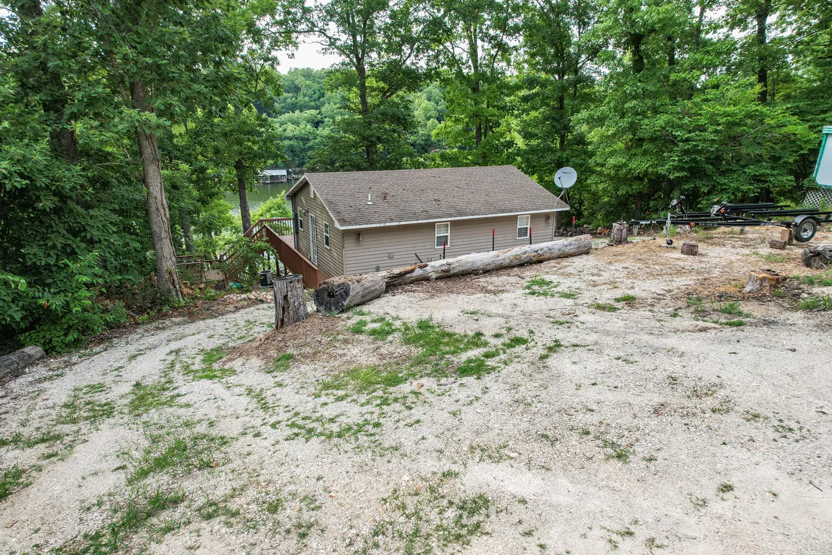 A wide exterior shot of the house surrounded by tall trees and logs on the ground, suggesting a natural, rustic setting ideal for outdoor activities. The scene hints at nearby woods and trails, aligning with the idea of nature walks and outdoor exploration with pets.