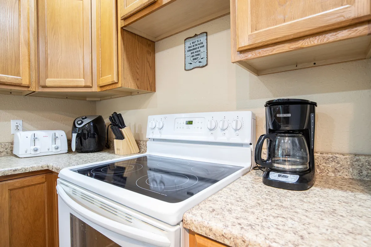 This image showcases a welcoming kitchen scene, including a stove, coffee maker, kitchen utensils, and a toaster. These elements evoke the feel of a well-stocked, functional space ideal for meal preparation and brewing fresh coffee. The inviting atmosphere hints at the presence of all the essentials, aligning with the 'Pack Less Program™' and making it easy for guests to cook and gather.