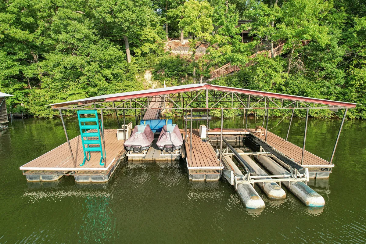 A private dock stretches out over calm lake waters, equipped with a swimming ladder and jet skis moored alongside. The dock is set in a quiet, wooded cove, providing both recreational access and a peaceful retreat.