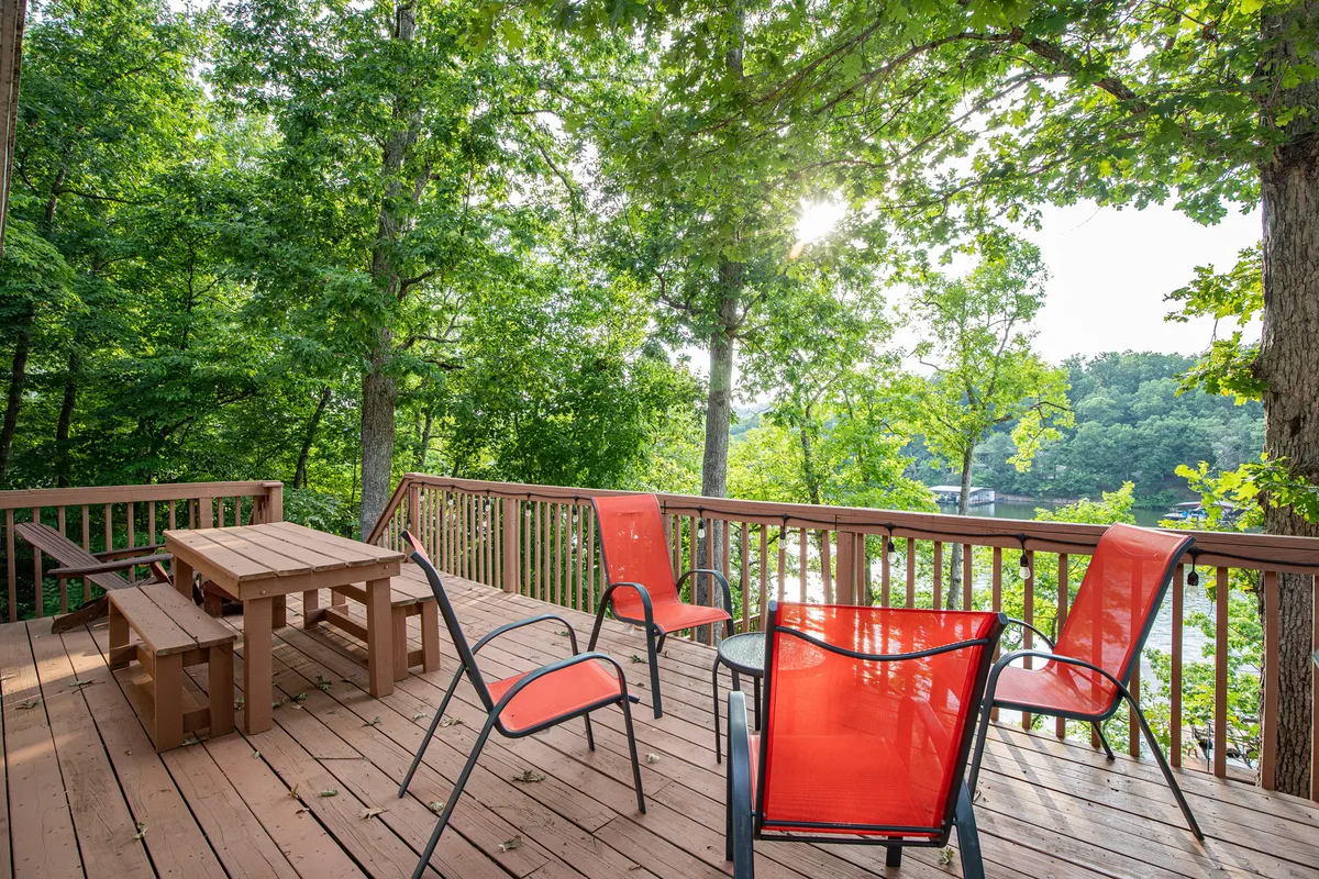 A wooden deck equipped with bright orange chairs overlooks the water and is surrounded by trees. The setup invites relaxation and socializing in a serene, natural setting, with easy access to outdoor fun and nearby trails.