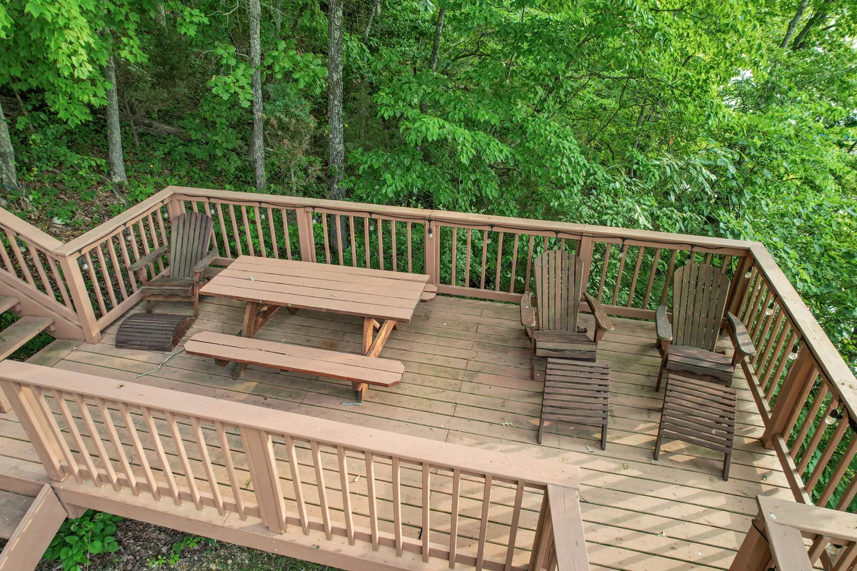 This exterior shot features a wooden deck with Adirondack chairs and a picnic table nestled among trees. The setup is perfect for relaxing, socializing, or enjoying morning coffee while immersed in nature.