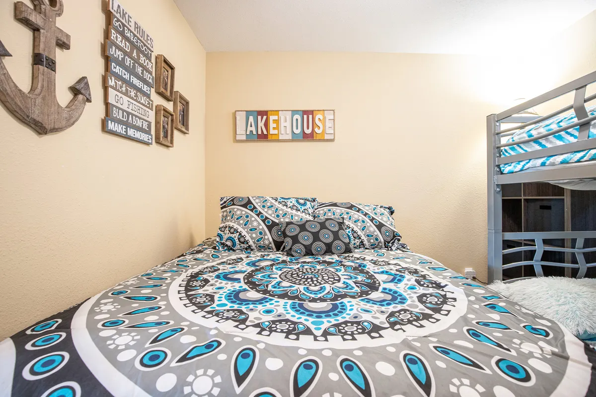 A bedroom scene with a queen bed, intricate bedding, anchor-themed decor, and a welcoming lakehouse sign. The room’s inviting atmosphere signals relaxation and comfort, with thoughtful details that create a peaceful haven after busy days outdoors.